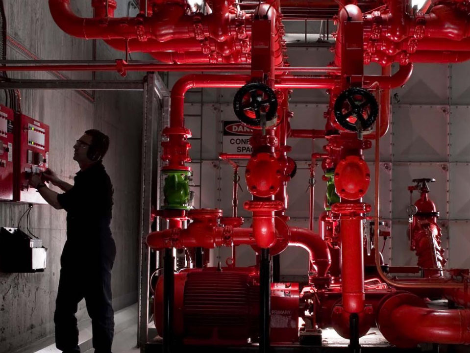 Person using a panel while standing near large red pipes.